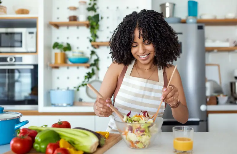 a woman in a kitchen mixing a salad