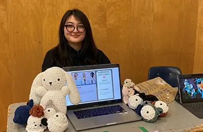 a woman sitting at a table with a laptop and stuffed animals