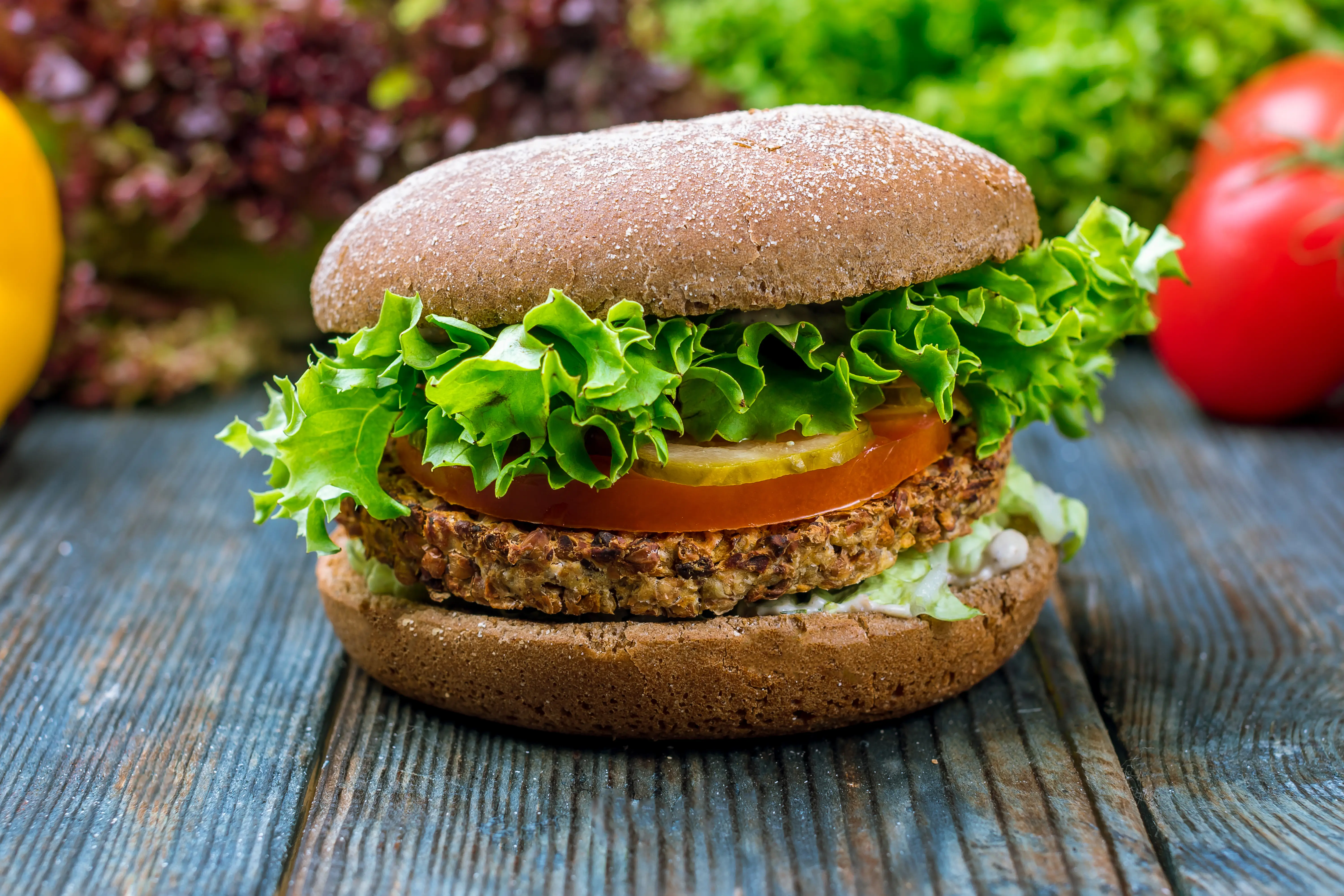 a burger with lettuce and tomato on a wooden surface