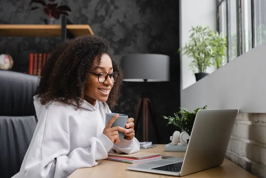 a woman holding a cup and looking at a laptop