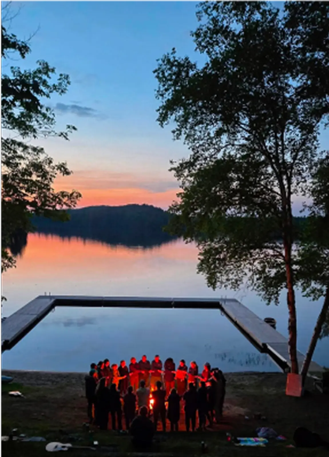 a group of people standing around a pool with trees and a sunset