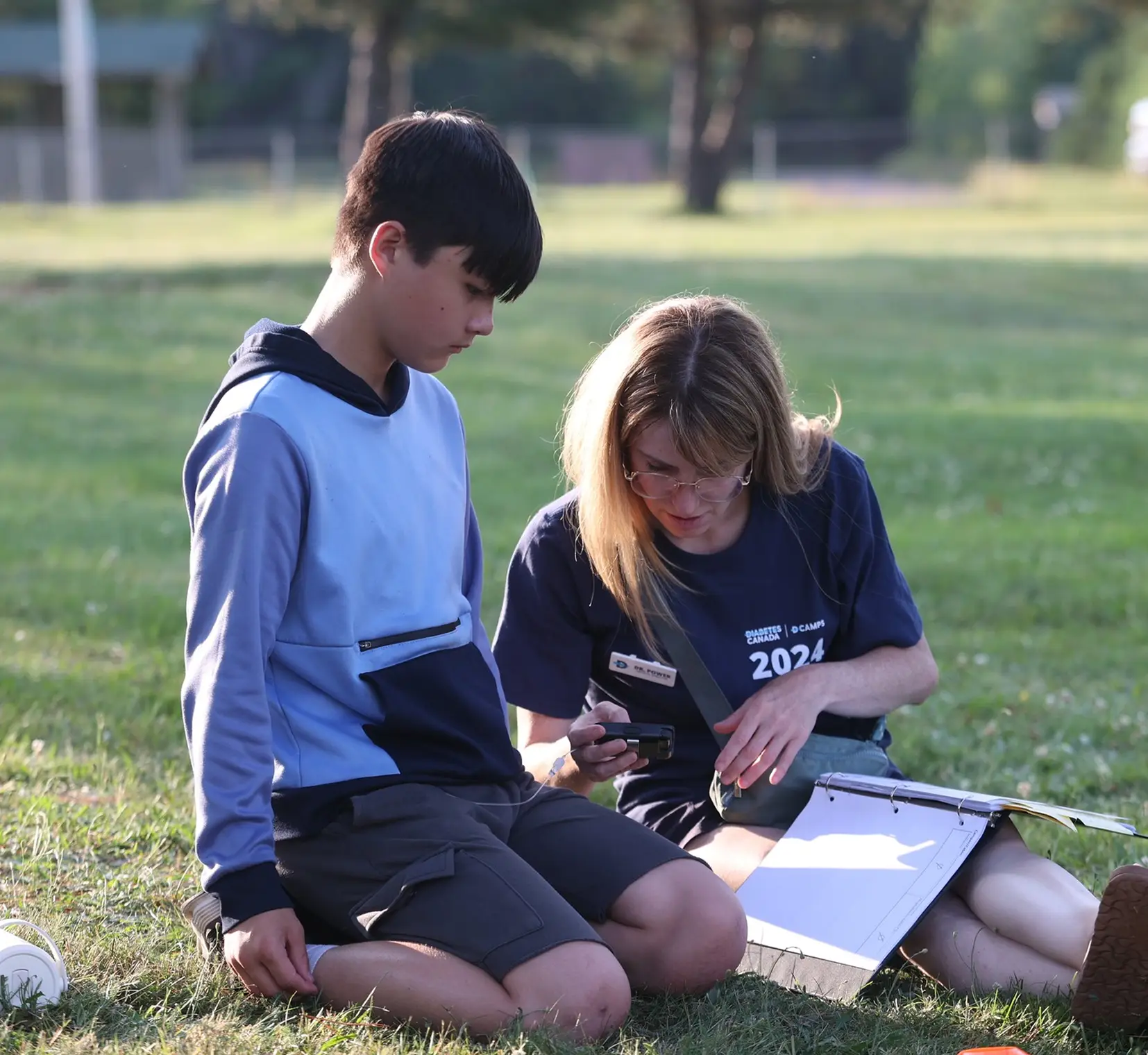 a boy and girl sitting on grass looking at a book