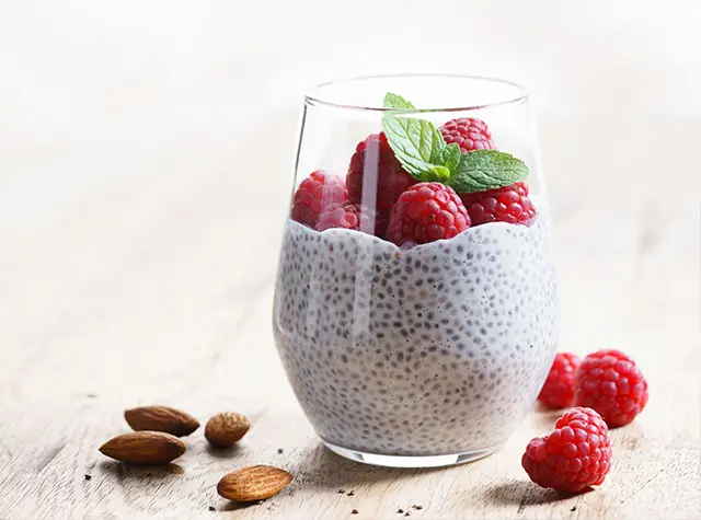a glass of chia pudding with raspberries and mint leaves