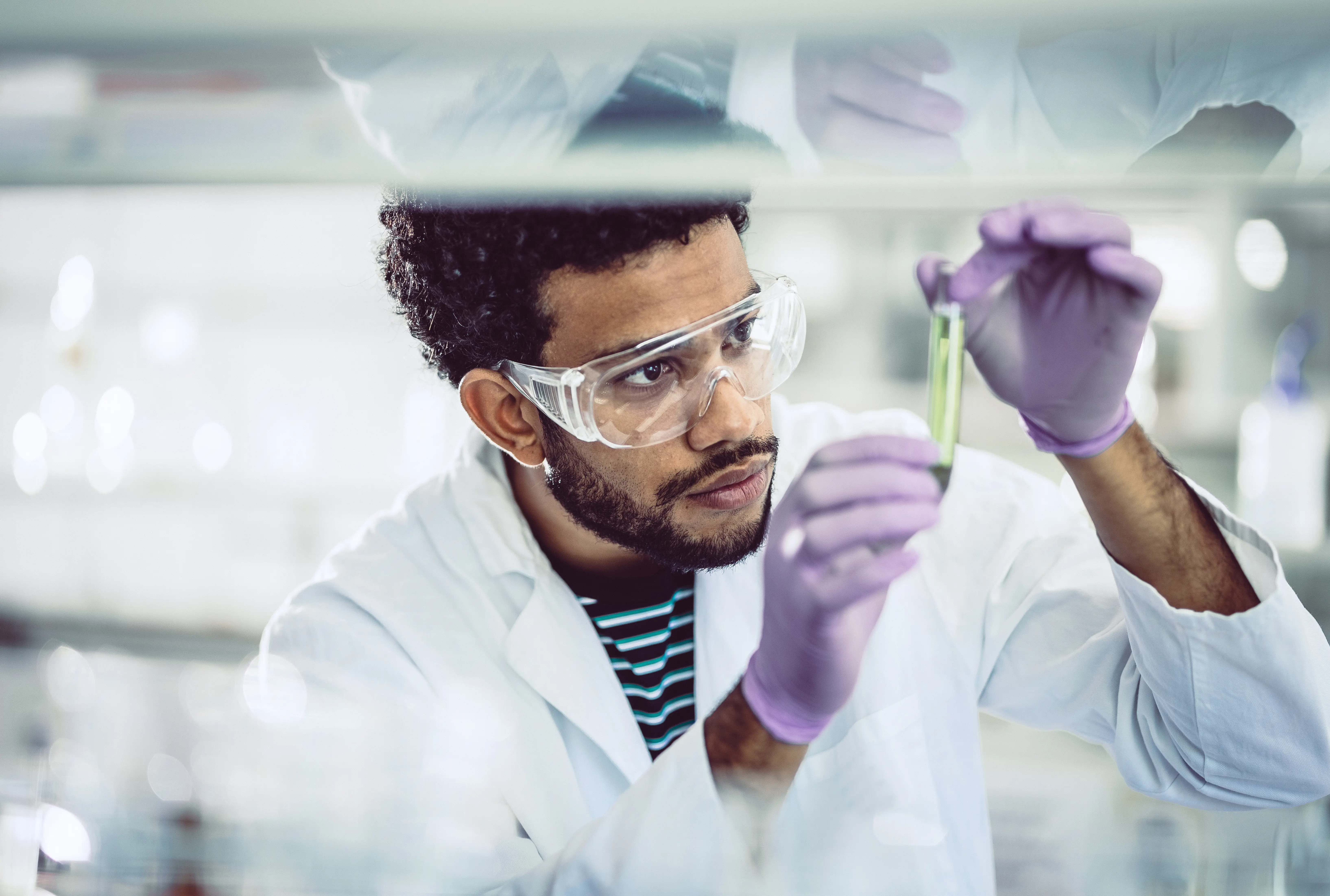 a man wearing goggles and white coat holding a test tube